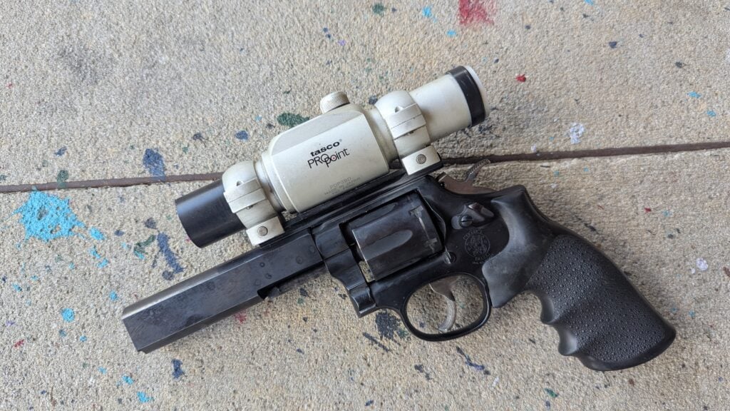 Revolver with a mounted optic marked 'Tasco Pro Point' on paint-splattered concrete